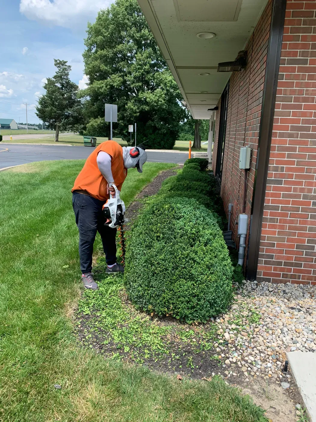 A JBH Landscaping crew member trimming a shrub beside a brick building