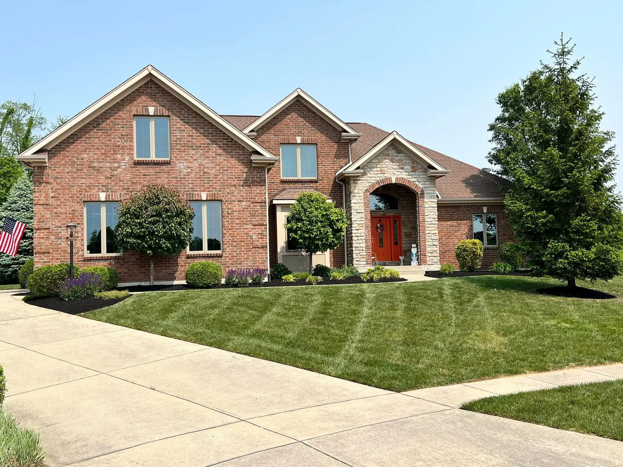 A two-story brick home with a red front door, mulched beds and a freshly mowed, striped lawn
