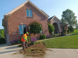 A crew member edging a bed in front of a brick home