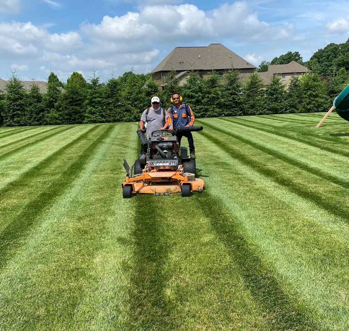 Two JBH Landscaping crew members mowing stripes into a large lawn