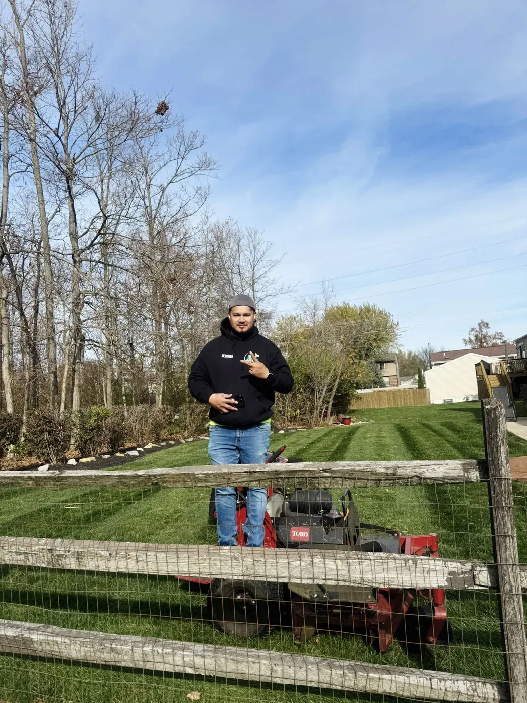 Jerson, owner of JBH Landscaping, standing behind a fence with his mower on a freshly striped lawn