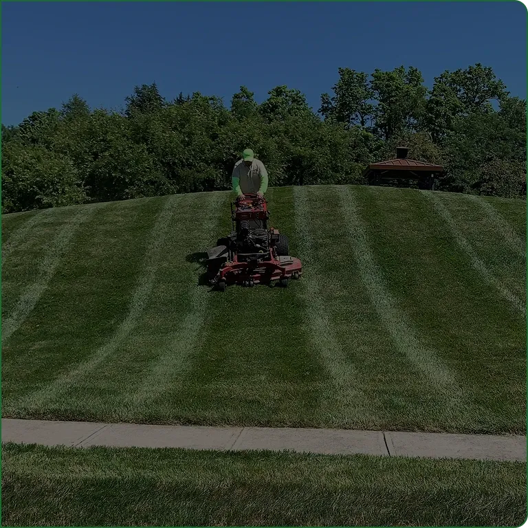 A JBH Landscaping crew member mowing a striped lawn in Dayton, Ohio