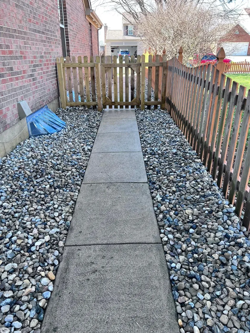A side yard with a wooden fence, river rock beds and a paver walkway