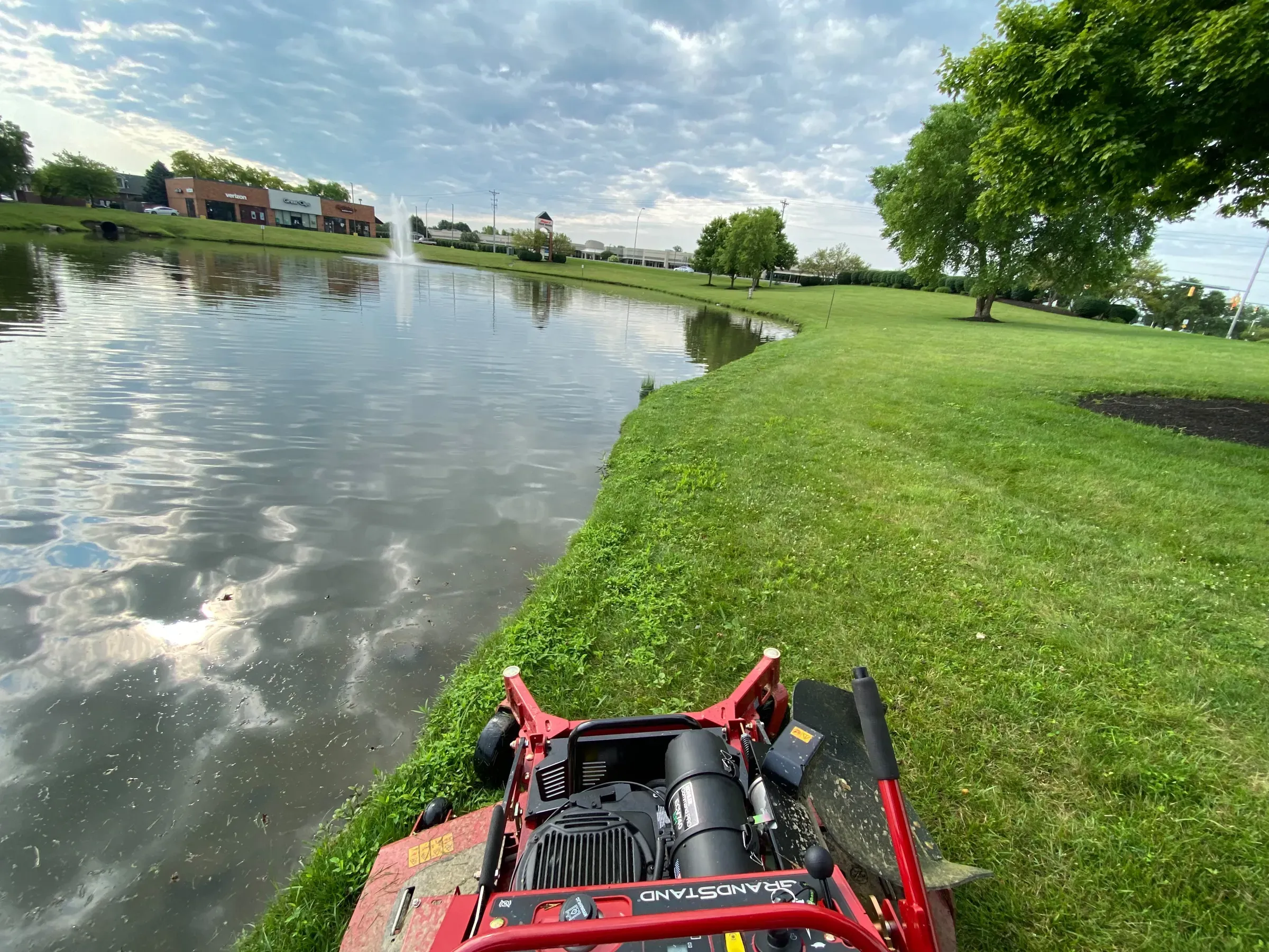 A JBH Landscaping stand-on mower cutting the grass along a pond bank in the Dayton area
