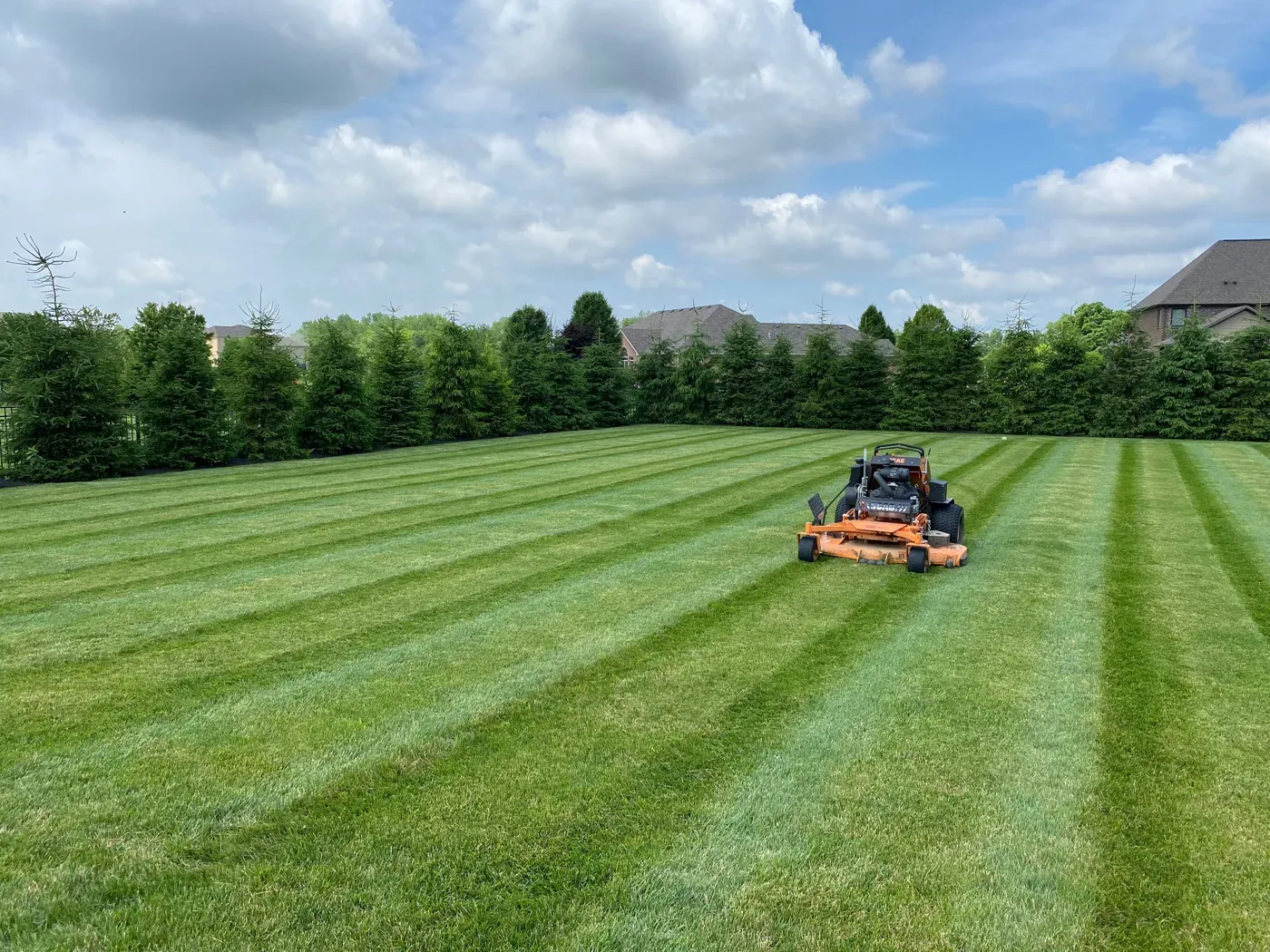 A zero-turn mower cutting stripes into a large backyard lawn